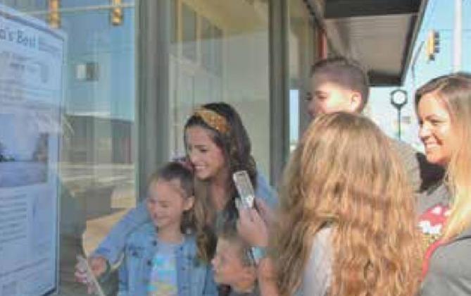 Left to right, Audrie Gholston, Lydia Gholston holding her cell, Henry Gholston, Gracen Hickman in back, and Emilie Hickman, with Eva Hickman in front holding her cell, use their Smart Phones to read the window display QR code on the corner of 5th and Main Streets in Yukon, to enter “Yukon’s Best History Contest.”
